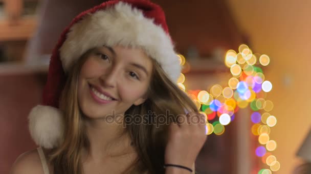 Красивая молодая женщина улыбается и смотрит в камеру в рождественской шляпе — стоковое видео
