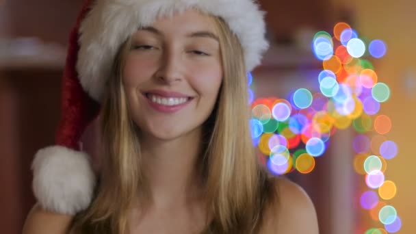 Una bella donna bionda con un cappello di Babbo Natale che soffia un bacio — Video Stock