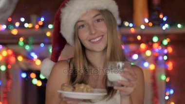 Kurabiye ve süt Noel Baba şapkası giyen güzel bir genç kadın sunar