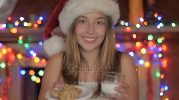 Красивая молодая женщина в санта-шляпе предлагает на Рождество кушанья и молоко — стоковое видео