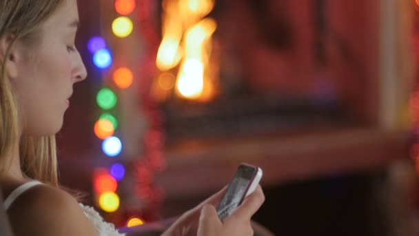 Une jeune belle adolescente est assise près d'un feu rugissant sur son téléphone intelligent - poupée 