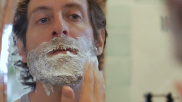 Ένας άνθρωπος με μια πλήρη γενειάδα ισχύει κρέμα ξυρίσματος για το πρόσωπό του-χειρός — Αρχείο Βίντεο