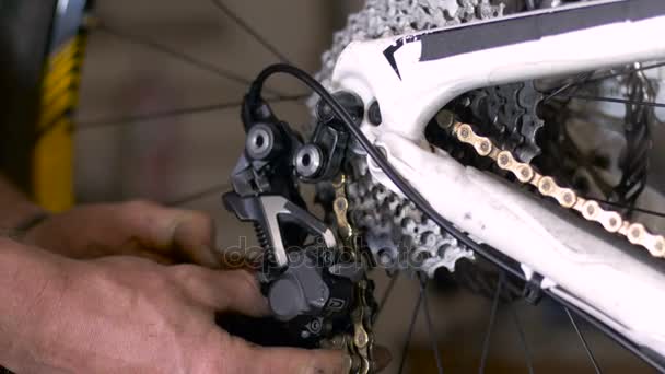 Un meccanico di biciclette infila una catena di biciclette attraverso un deragliatore con le mani — Video Stock