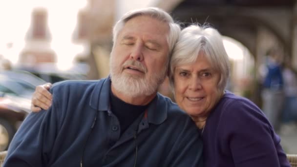 Una feliz pareja de ancianos se abraza y sonríe a la cámara de afuera en un café — Vídeo de stock