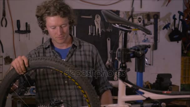 An attractive millennial man stands next to a bicycle in his workshop and smiles — Stock Video