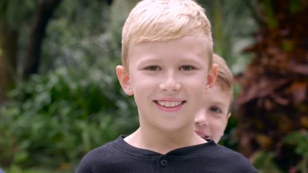 Een jonge jongen verschuilt zich achter zijn oudere broer en geeft de duimen op elkaar — Stockvideo