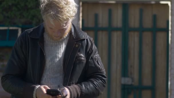 Een jongeman duizendjarige SMS op zijn mobiele telefoon buiten het dragen van een jas — Stockvideo