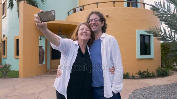 An older couple take photos of themselves in front their new house — Stock Video