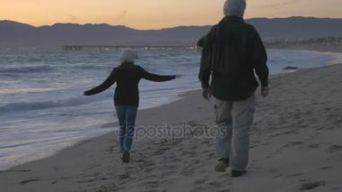 Çalışan ve gün batımında sahilde oynarken mutlu olgun 60'ların Çift