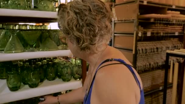 A woman in her 60s deciding on two different glasses while shopping — Stock Video