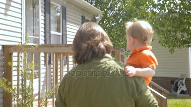 Любящий отец, идущий и несущий своего маленького сына к своему дому — стоковое видео