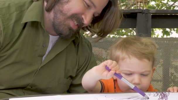 Ein stolzer Vater beobachtet seinen kleinen Jungen beim Färben mit einem Filzstift in Zeitlupe — Stockvideo