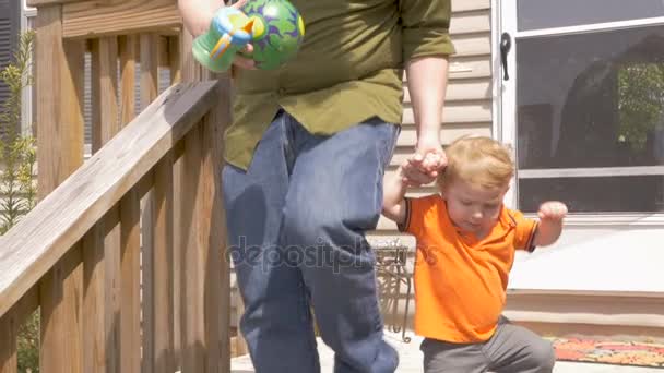 Un padre joven sostiene a su hijo pequeño de la mano y lo ayuda a caminar por los escalones — Vídeo de stock