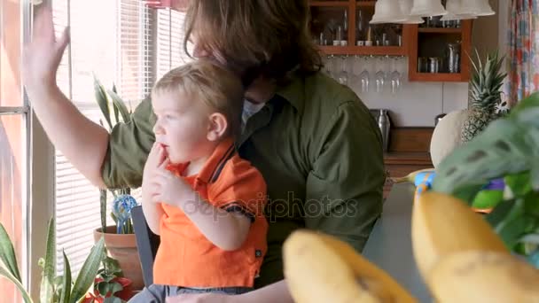 Un padre se despide mientras su pequeño hijo se sienta en su regazo comiendo un bocadillo — Vídeos de Stock