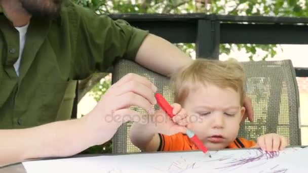 Um pai amoroso beija seu filho criança jovem enquanto ele desenha no papel fora — Vídeo de Stock