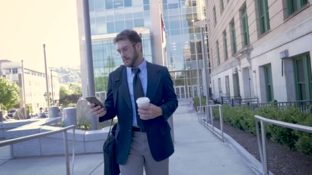 Millennial hombre de negocios caminando con teléfono inteligente lo convierte en horizontal — Vídeo de stock