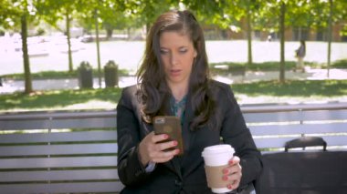 Gülümseyen ve akıllı telefon - pushin üzerinde kahve içme parkta bankta oturan kadın