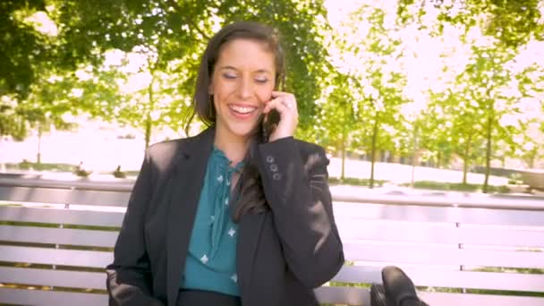 Feliz sorrindo mulher milenar trabalhando e falando no telefone inteligente no banco do parque — Vídeo de Stock