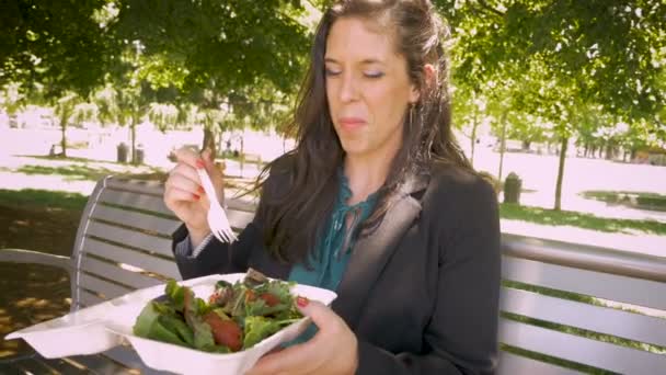 Mujer joven comiendo ensalada saludable en contenedor biodegradable para llevar en el parque — Vídeos de Stock