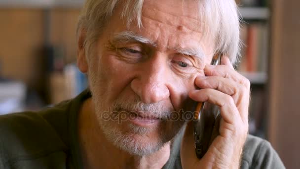 Schöner älterer Mann, der in seinem Haus auf einem Smartphone-Mobilgerät spricht — Stockvideo