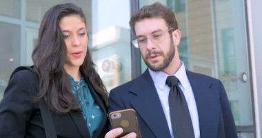 Bir iyi giyimli erkek ve kadın gülümseyerek ve dışarıda konuşmaya akıllı telefon bakarak