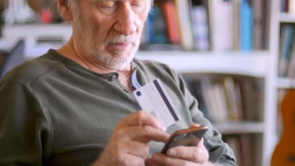 ハンサムな年配の男性のクレジット カードでオンラインで彼の携帯電話上の順序 — ストック動画