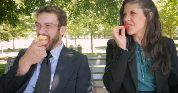 Üzleti partnerek érett gyümölcsöt eszik ülve egy park padon odaad-tartott — Stock videók