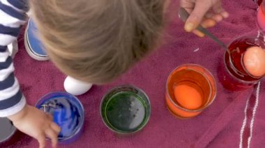 Genç bir çocuk annesi Paskalya yumurtaları tatil kutlaması için boyama yardımcı olur.