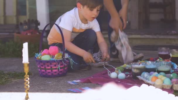 Mère millénaire et jeune fils colorier des oeufs de Pâques ensemble à l'extérieur — Video