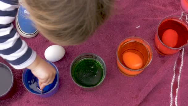 Cute little girl using her hands to grab an easter egg out of blue dye — Stock Video