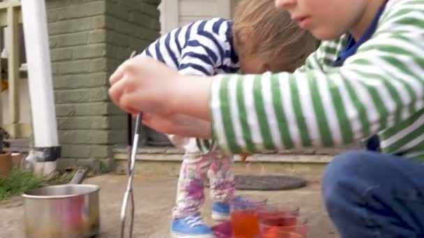 Двое маленьких детей вместе рисуют и красят пасхальные яйца на улице — стоковое видео