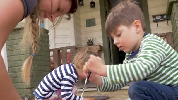 Eine tausendjährige Mutter und ihre beiden kleinen Kinder beim gemeinsamen Färben von Ostereiern — Stockvideo