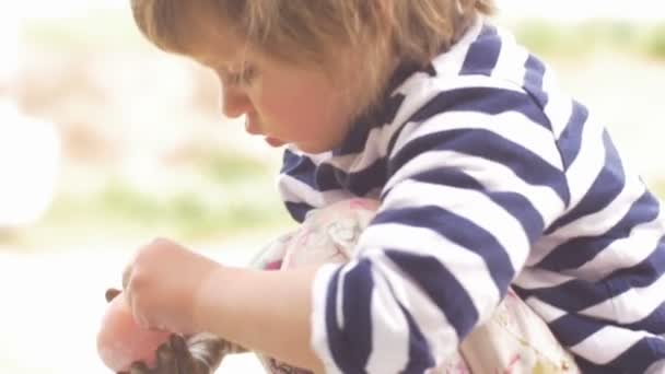 Маленькая девочка играет с чем-то в руке на улице в замедленной съемке — стоковое видео