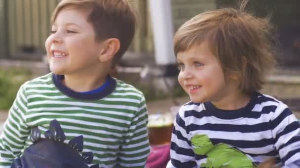 Двое возбужденных маленьких детей улыбаются и смотрят в ожидании снаружи — стоковое видео