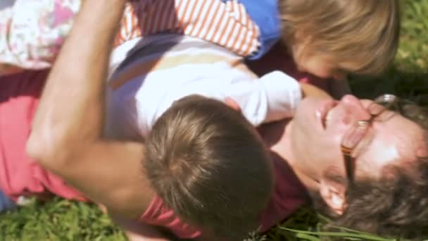 Un père et ses deux enfants rient et se roulent dans l'herbe ensemble — Video