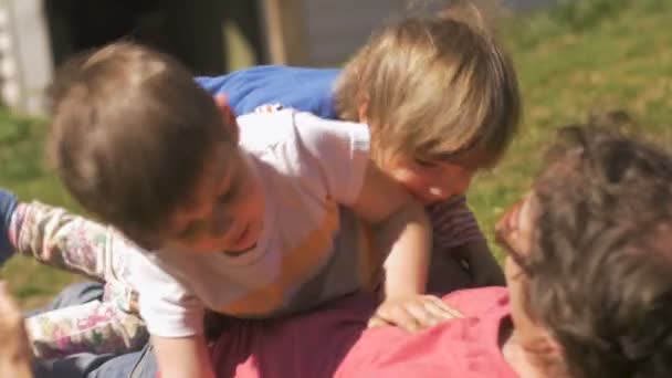 Девочка и мальчик борются и лежат на своем отце в траве — стоковое видео
