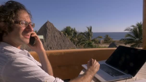 Homem falando no telefone inteligente enquanto trabalhava no escritório em casa na praia — Vídeo de Stock