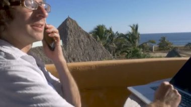 Okyanus Manzaralı akıllı telefona cevap için dizüstü bilgisayarda çalışan dijital göçebe adam durur