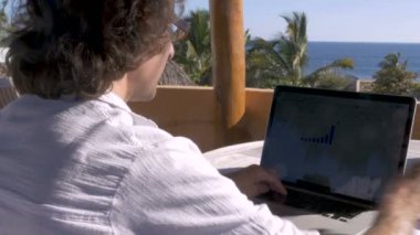 Adam dışarıda ev ofis dizüstü bilgisayarda okyanus manzaralı çalışırken kahve içer