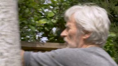 Happy active retired senior man rebuilding a broken fence in his yard