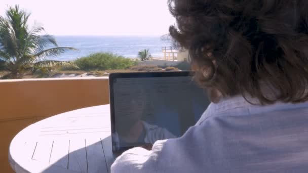 Mężczyzna pracujący w arkuszu kalkulacyjnym na komputerze w domu z ocean view dolly strzał — Wideo stockowe