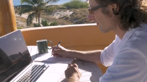 チャートやグラフをコンピューターで作業をペンと紙で書く男 — ストック動画
