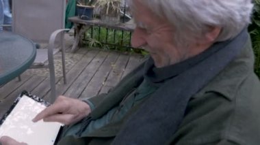 Profil yaşlı bir üst düzey adamın onun tablet üzerinde kaydırma sırasında gülüyor