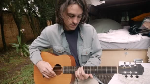 Bonito hipster millennial homem tocando guitarra enquanto sentado em seu campista — Vídeo de Stock