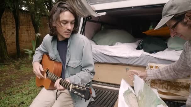 Чоловік складає карту зі своїм другом під час кемпінгу на вулиці під час подорожі — стокове відео