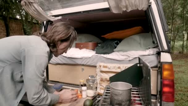 Joven poniendo comida en una estufa de campamento preparando su cena — Vídeos de Stock