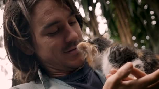 Счастливый улыбающийся и смеющийся привлекательный мужчина держит крошечного котенка у своего лица — стоковое видео