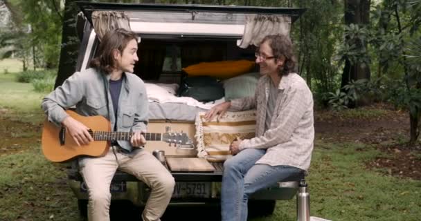 Deux hommes aux cheveux longs et à la guitare parlent et s'assoient sur le hayon d'un camion — Video