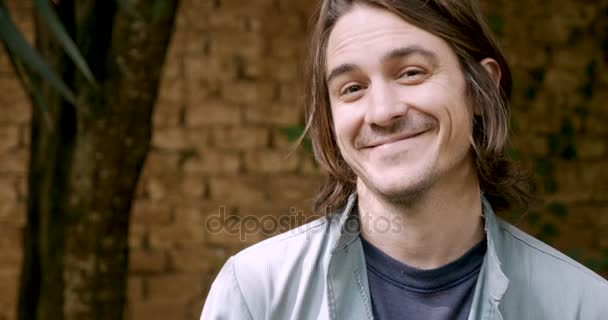 Jóképű férfi, hosszú haj, és mosolyogva néz a kamerába — Stock videók