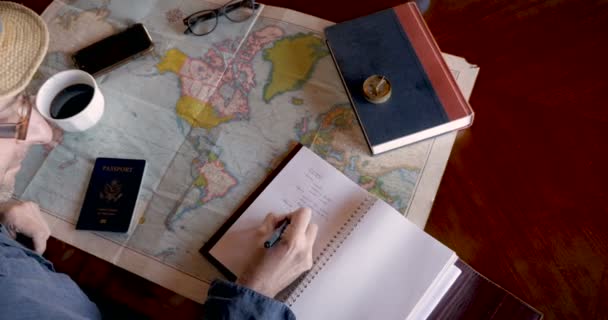Overhead of young man planning a travel trip with coffee, notebook, and map — Stock Video